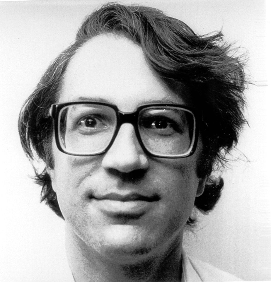 Black and white portrait of Peter J. Weinberger: a man with tousled hair and large square glasses, smiling slightly at the camera